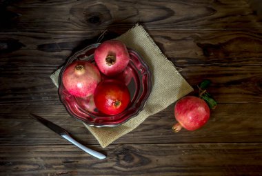 Olgun, büyük, tatlı, kırmızı nar tabakta ve yakın plandaki tahta masada bir bıçak.