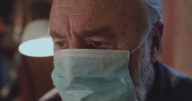 Tıbbi maskeli terli yaşlı adamın portresi alnını peçeteyle siliyor.