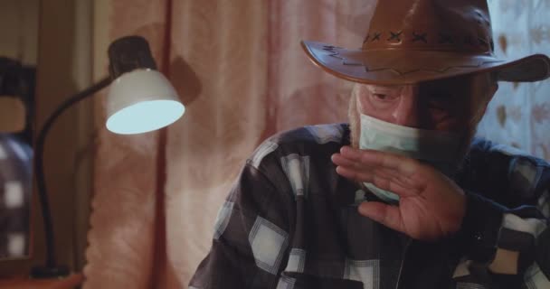 Старший в шляпе снимает медицинскую маску и сильно кашляет. — стоковое видео