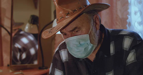 Portrait of ill senior man in hat and medical mask looks at camera with sadness Stock Image