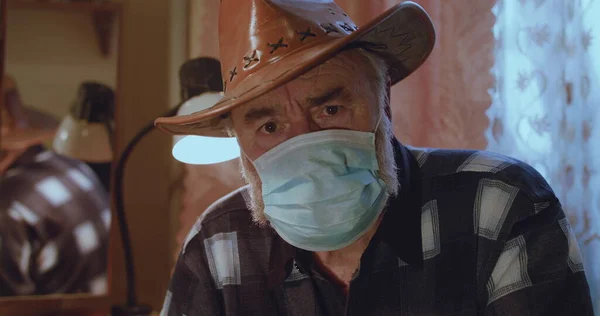 Şapkalı ve tıbbi maskeli yaşlı bir adamın portresi hüzünle kameraya bakıyor. Telifsiz Stok Imajlar