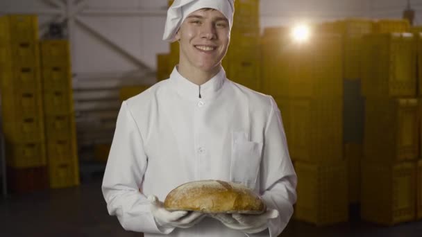 身穿制服的快乐面包师在有背光的面包店里放着一块新鲜的面包 — 图库视频影像