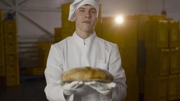 Пекарь в форме представляет перед камерой свежеиспеченный хлеб в пекарне — стоковое видео