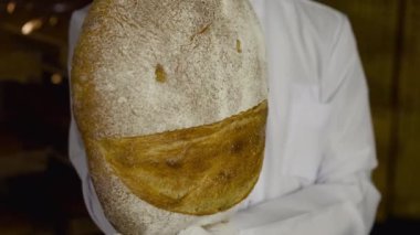 Büyük yuvarlak ekmek somununun görüntüsü fırıncının elinde kameraya gülümseyişin görüntüsü