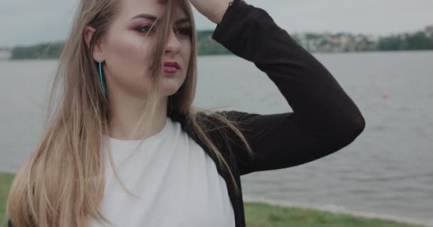 Tineri, fata zâmbitoare corectează suflarea părului atunci când se uită deoparte pe litoral — Videoclip de stoc