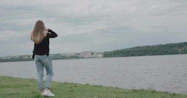 Mutlu kız deniz kenarında yürüyor, kameraya dönüyor, saçlarıyla poz veriyor ve gülümsüyor.