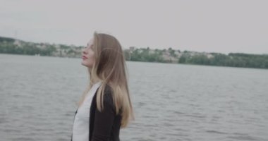 Rüzgâr sırasında nehir kenarında yürüyen çekici kız, neşeli ve kolayca poz veriyor.