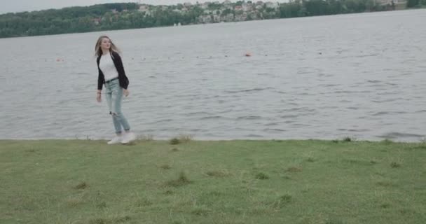 Chica alegre abrazándose del frío durante el viento en un paseo por el río — Vídeos de Stock