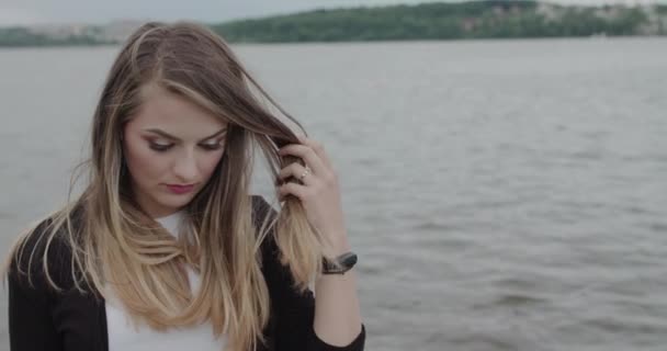 Gadis bijaksana mengoreksi rambut bertiup dan tersenyum di kamera di jalan-jalan di sungai — Stok Video