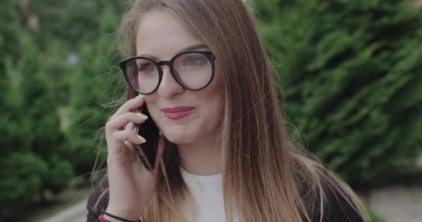 Retrato de una jovencita feliz con gafas hablando por teléfono con sonrisa en la cara — Vídeos de Stock