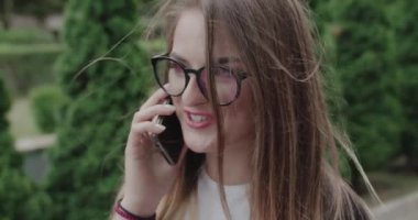 Mutlu, gözlüklü genç kız saçlarını savurarak telefonda gülümsüyor.