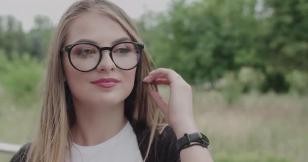 Όμορφη κοπέλα με φυσώντας τα μαλλιά διορθώνει τα γυαλιά εύκολα και κοιτάζοντας στην κάμερα — Αρχείο Βίντεο