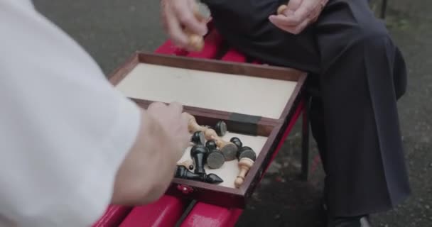 Vista baixa de dois idosos homens preparando o tabuleiro de xadrez antes do jogo no banco de rua — Vídeo de Stock