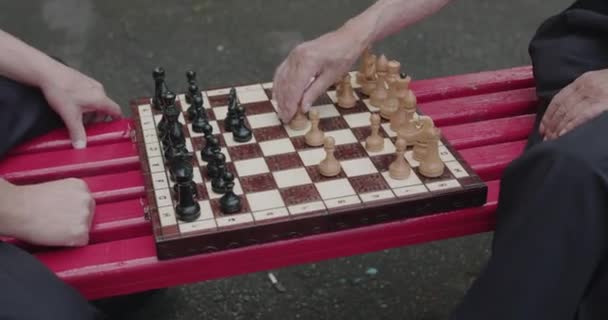 Close view of two seniors hands playing the chess on street bench on leisure — Wideo stockowe