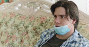 Sıkıcı izolasyondan bıkmış, televizyon kumandası kullanıyor, maskesini indiriyor ve kameraya bakıyor.