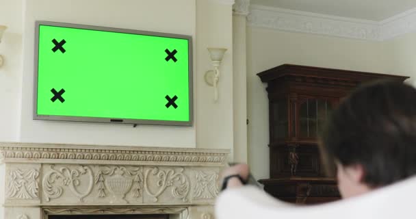 Человек переключает каналы с пульта телевизора с зеленым экраном дома — стоковое видео