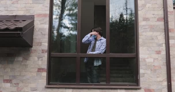 Мужчина прислонился к окну, огляделся, выбрасывает маску и дышит свежим воздухом — стоковое видео