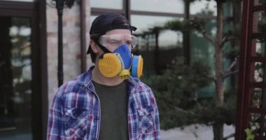 Koruyucu gözlüklü ve evrensel solunum cihazlı bir adam kameraya bakar.