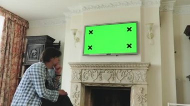 Evdeki izole adam yeşil ekranlı bir plazma TV izler ve kafasını sallar.