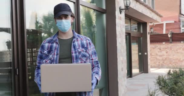 Homem usado em máscara e luvas com pacote em mãos em casa olha para a câmera — Vídeo de Stock