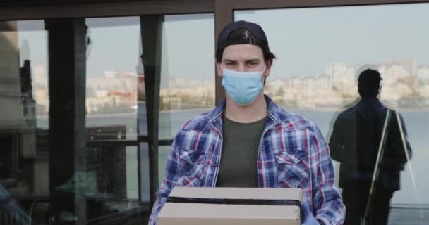 Mann mit Maske und Handschuhen zieht ein Paket in Karton vor die Kamera und zurück — Stockvideo