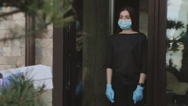Изолированная девушка в маске получает безопасную доставку заказа при входе в дом — стоковое видео