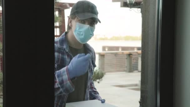 Кур'єр у масці стукає у двері будинку, щоб передати порядок жінці-клієнту — стокове відео
