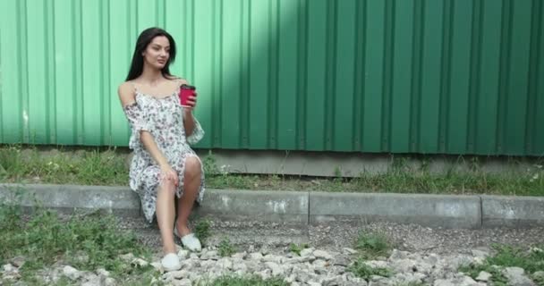 Wanita cantik berpakaian terang dengan secangkir minuman duduk di perbatasan — Stok Video