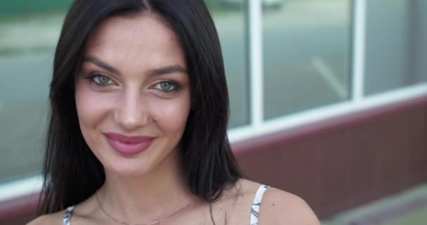 Enigmatická brunetka opravuje své vlasy a usmívá se na kameru na ulici — Stock video