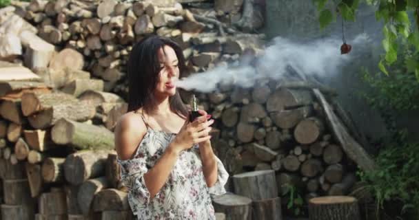 Ładna dziewczyna palenie e-papierosa i wydycha odparowanie na charakter drewna — Wideo stockowe
