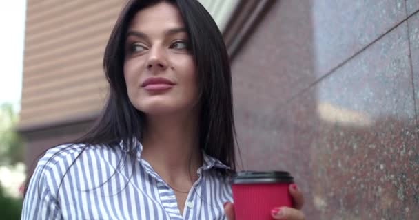 Красивая брюнетка держит чашку кофе, думая, исправляя волосы и улыбаясь — стоковое видео
