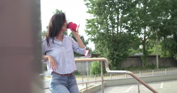 Stylish lady leaned on stairs handrail, drinks a beverage and poses with hair — Stock Video