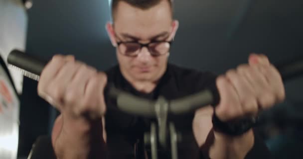 Gözlüklü bir sporcunun ön görüntüsü kol kaslarını çalıştırmak için simülatörle çalışır — Stok video
