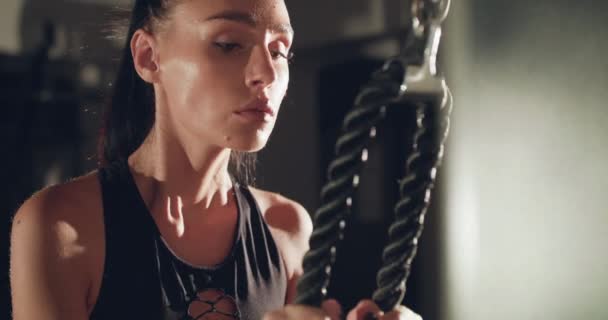 Konsantre kadın sporcunun spor salonundaki simülatörde halatla çubuğu çekiş görüntüsü — Stok video