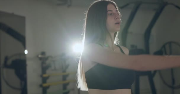 Молода дівчина в спортивному одязі зігріває руки і торс під час роботи в спортзалі — стокове відео
