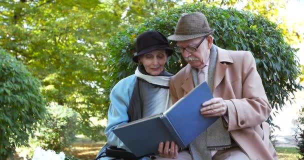 Porträt eines älteren Ehepaares, das es sich auf einer Parkbank gemütlich macht und ein Fotoalbum betrachtet — Stockvideo