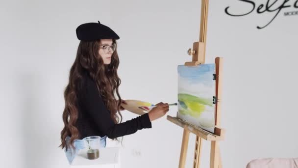 Young woman artist in beret painting picture on canvas in art studio — Stock Video