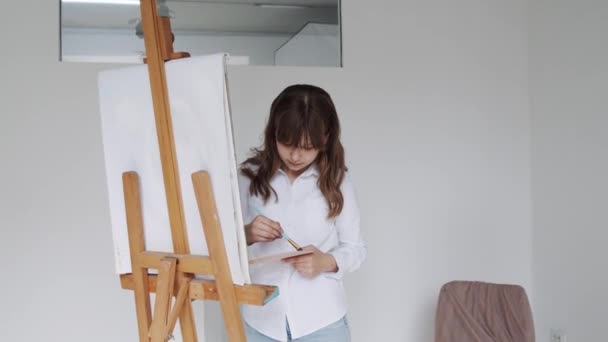 Jong meisje kunstenaar schilderij schilderij op doek in kunst studio — Stockvideo