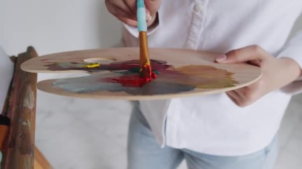 Detailní záběr kresby woomanových rukou štětcem a paletou s barevnými barvami na stojanu uvnitř. — Stock video