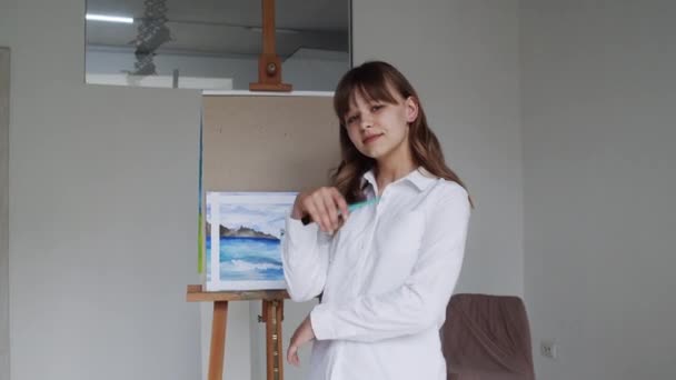 Retrato de artista feliz posando cerca de caballete con dibujo completado después de trabajar mirando a la cámara — Vídeo de stock