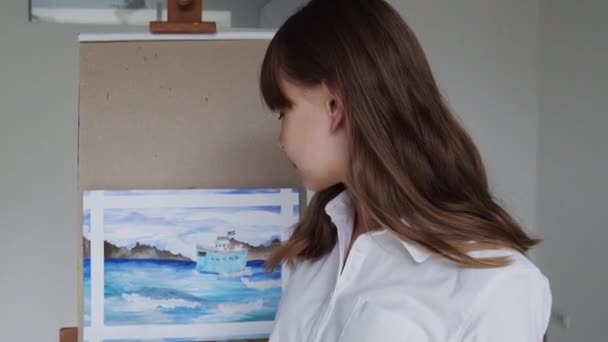 Крупним планом портрет щасливої художниці-жінки позує біля мольберта з завершеним малюнком після роботи, дивлячись на камеру — стокове відео
