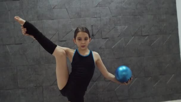Дівчина-підліток робить розкол і тримає блакитний м'яч — стокове відео