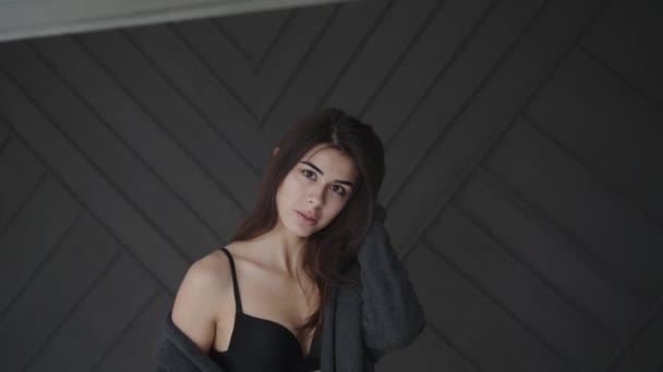 Seductive brunette in black lingerie corrects her hair and smiles in studio — Stockvideo