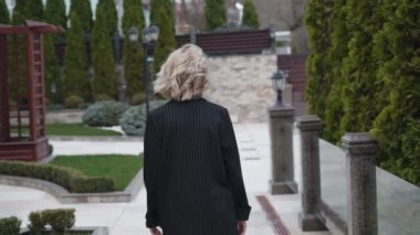 Takım elbiseli şık bir model rüzgarlı bir günde yürüyor, kameraya poz veriyor ve flört ediyor.