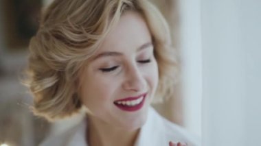 Kırmızı dudaklı mutlu bayanın portresi aydınlık odada kameraya poz veriyor.