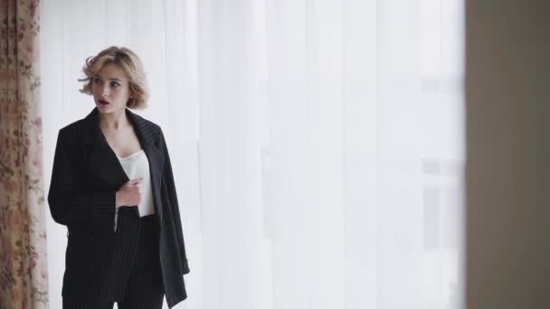 Portrait of proud woman in suit poses and looks through the light window — Stockvideo