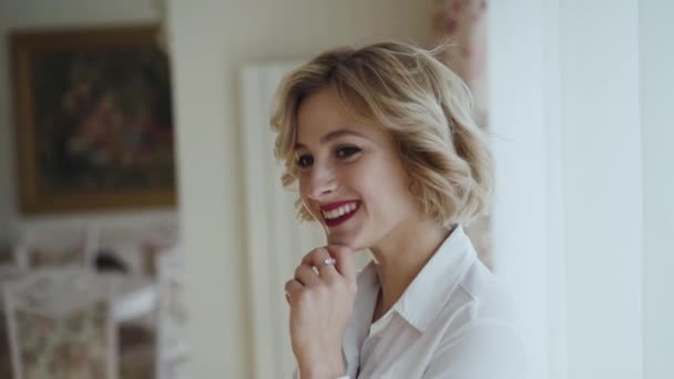 Portrait of happy lady with red lips rejoices at camera in light room — стоковое видео