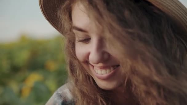 Portrait of smiling, pretty girl in hat with blowing long hair among sunflowers — Stockvideo