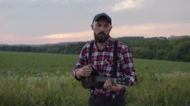 Çekici sakallı genç adam gitar çalıyor.