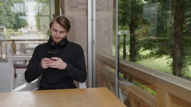 Молодий чоловік тримає пристрій смартфона смс-повідомлення, що сидить на стільці — стокове відео
